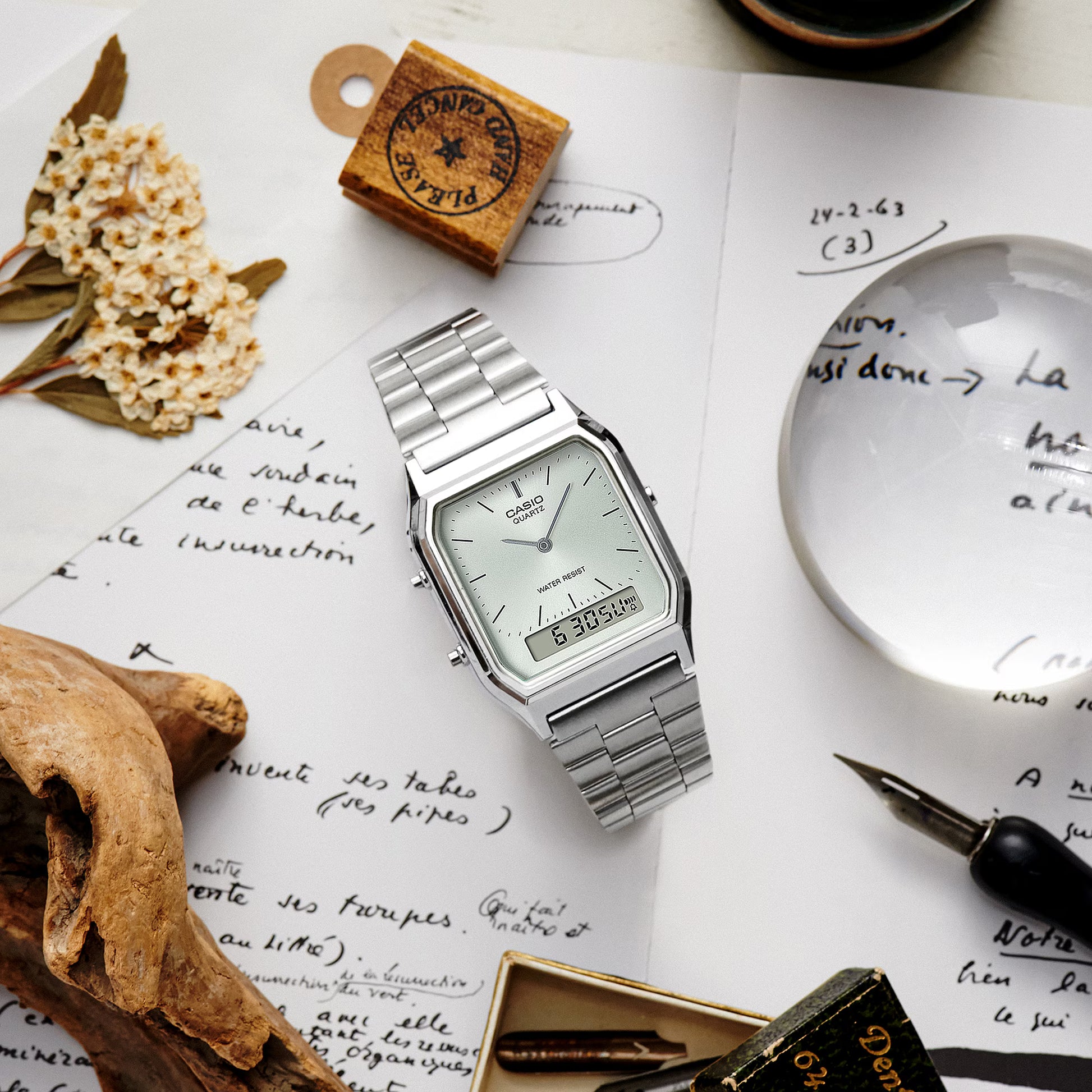 Silver watch on a surface with handwritten text, dried flowers, and a magnifying glass.