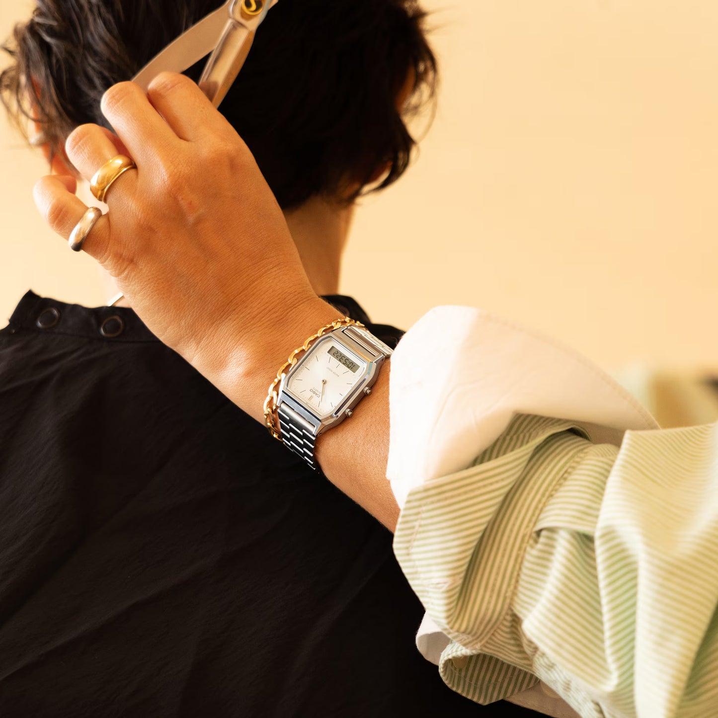 Person cutting hair with scissors, wearing a watch and ring.