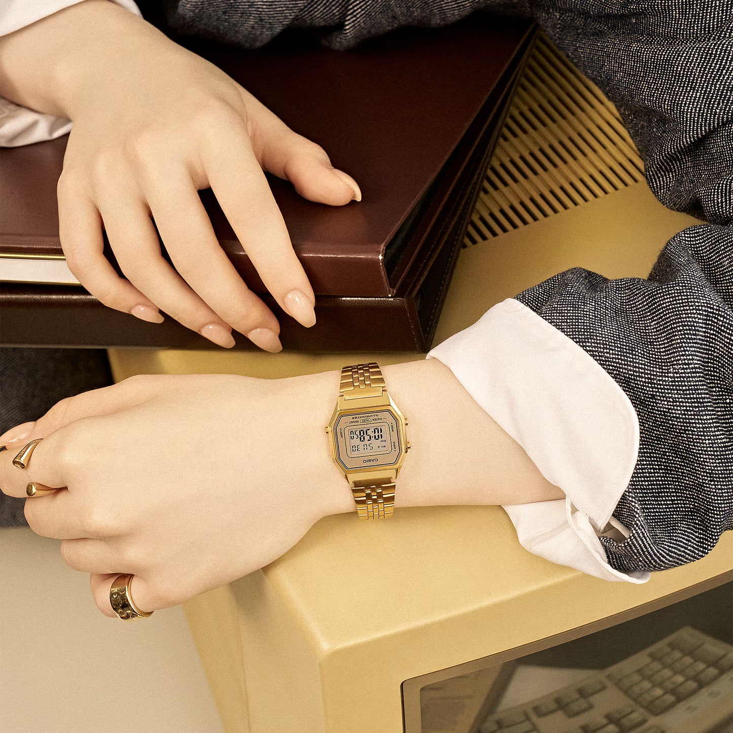 Person wearing a gold digital watch with a brown box in the background