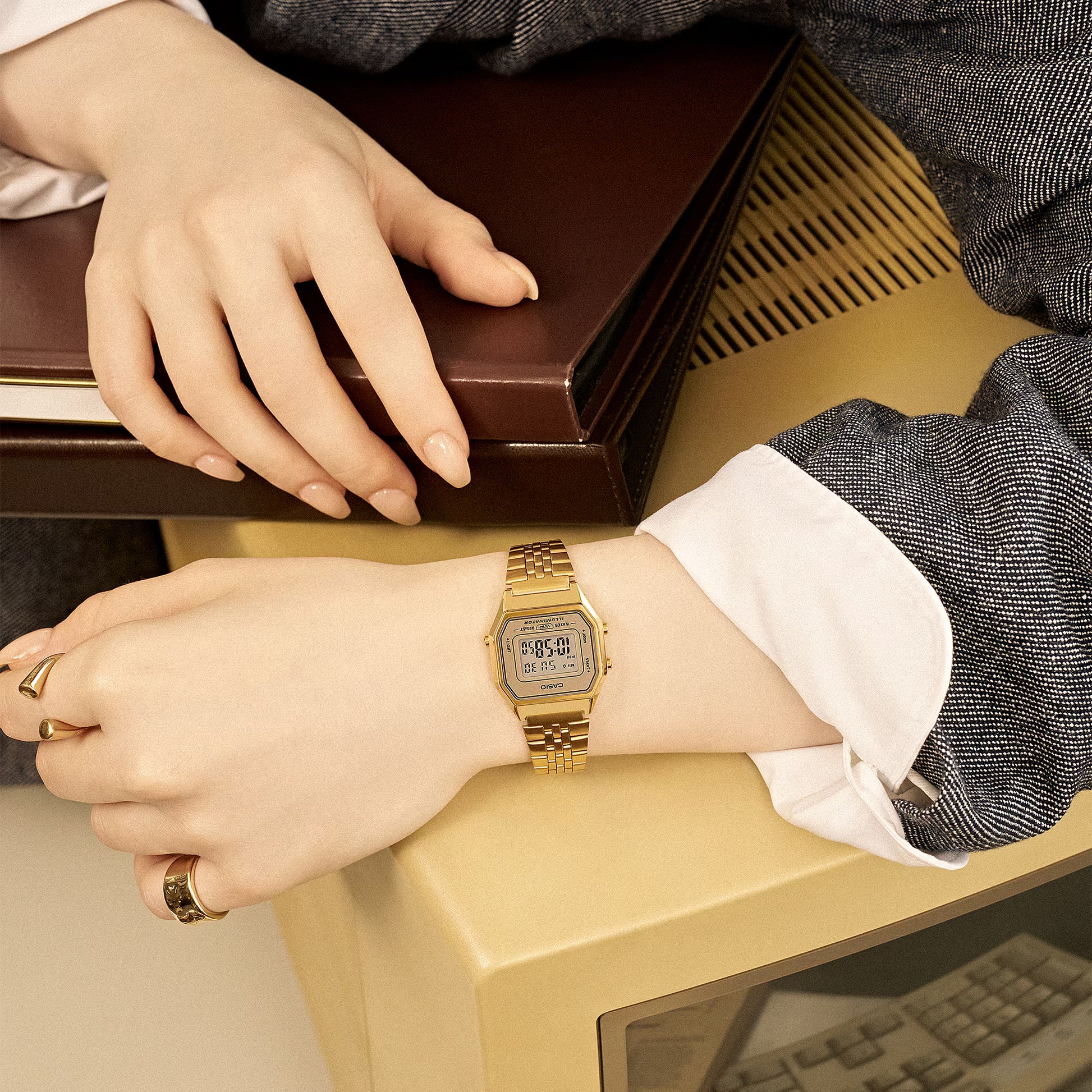 Person wearing a gold digital watch with a brown box in the background