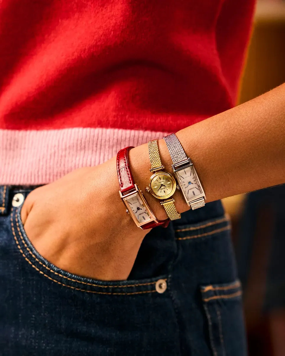 Close-up of a wrist wearing multiple watches and bracelets with a red sweater background.