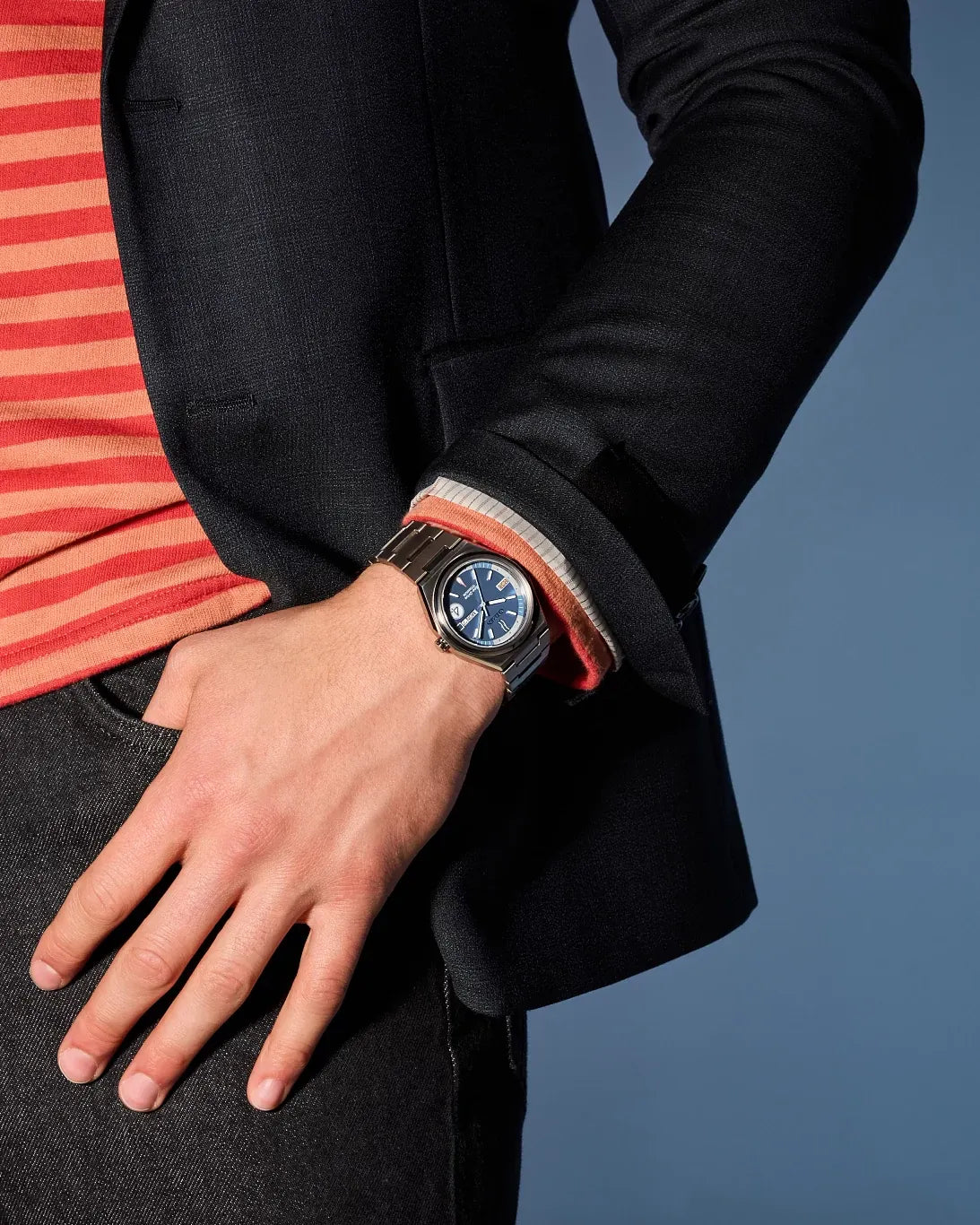 Lifestyle image of the Citizen Fantastic 4 AW0131-66W worn with a black blazer and striped shirt, featuring the blue dial and silver-tone Super Titanium bracelet.