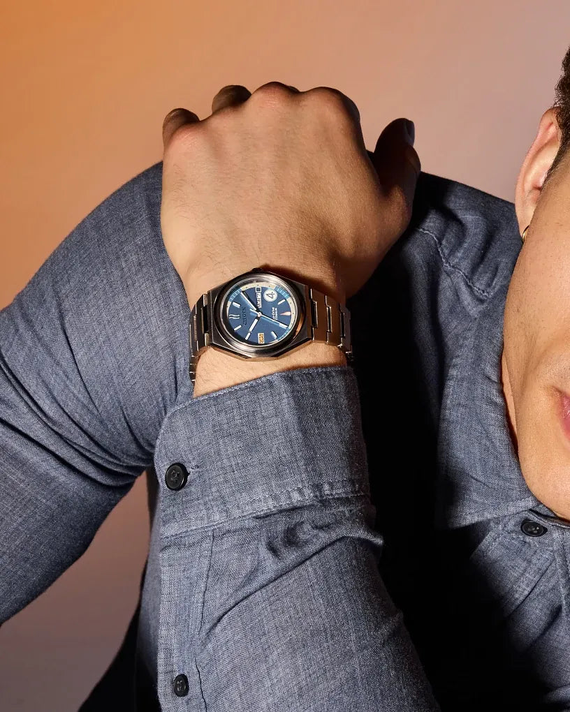 Citizen Fantastic 4 AW0131-66W worn on wrist with a blue shirt, showing the brushed blue dial, luminous markers, integrated bracelet, and polished everyday styling.