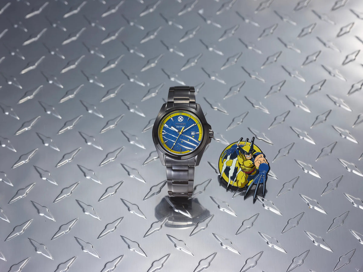 Citizen Marvel Wolverine AW1435-66W Eco-Drive watch displayed with matching Wolverine pin on a metal claw-pattern background, featuring blue dial, yellow outer ring, and black stainless steel bracelet