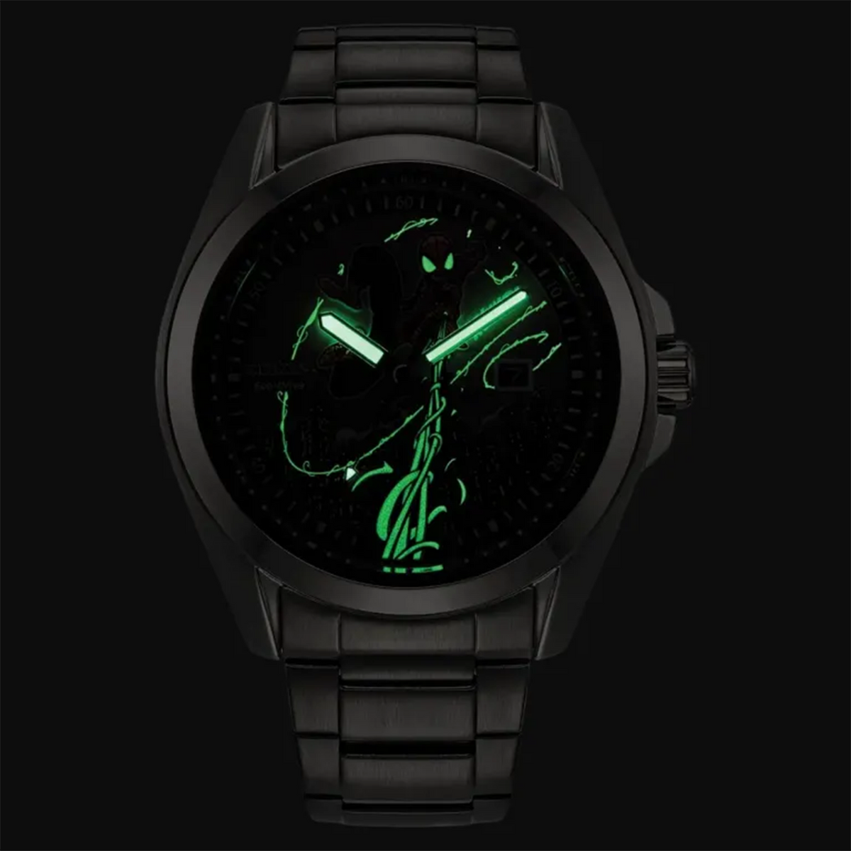 A black analog watch with a matching black metal link bracelet, shown against a dark background. The watch face is illuminated to reveal glowing green hands and a green graphic design on a black dial.