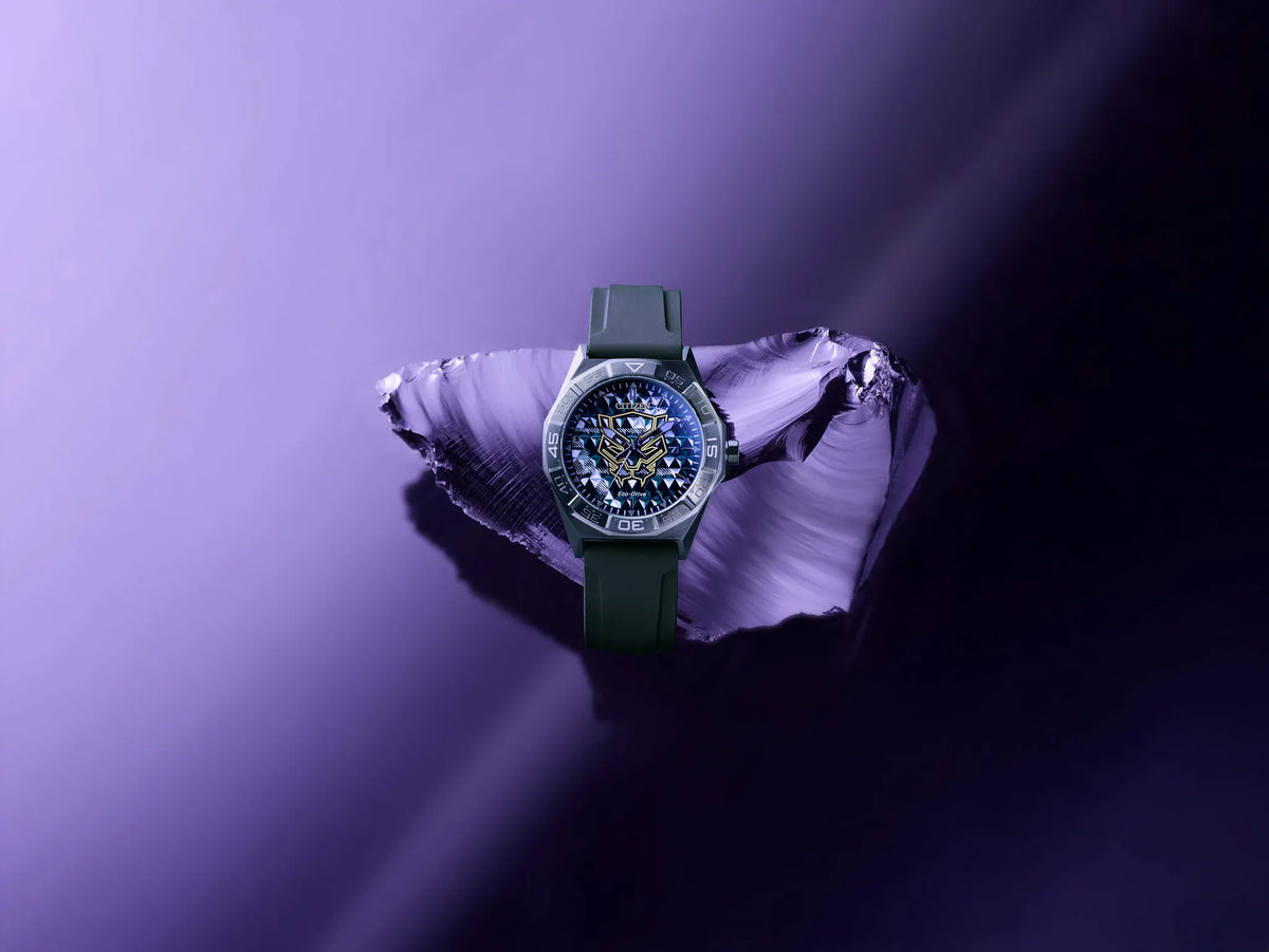 Citizen Black Panther 60th Anniversary AW1858-03W Eco-Drive watch with dimensional black dial, gold Black Panther mask logo, purple minute track, 42mm black IP stainless steel case, black silicone strap, sapphire crystal, and 100m water resistance.