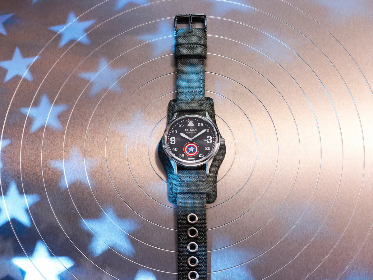 Citizen Captain America Forever BV1140-00W displayed on a target-inspired background with blue star lighting, featuring the shield sub-dial and rugged cuff strap.