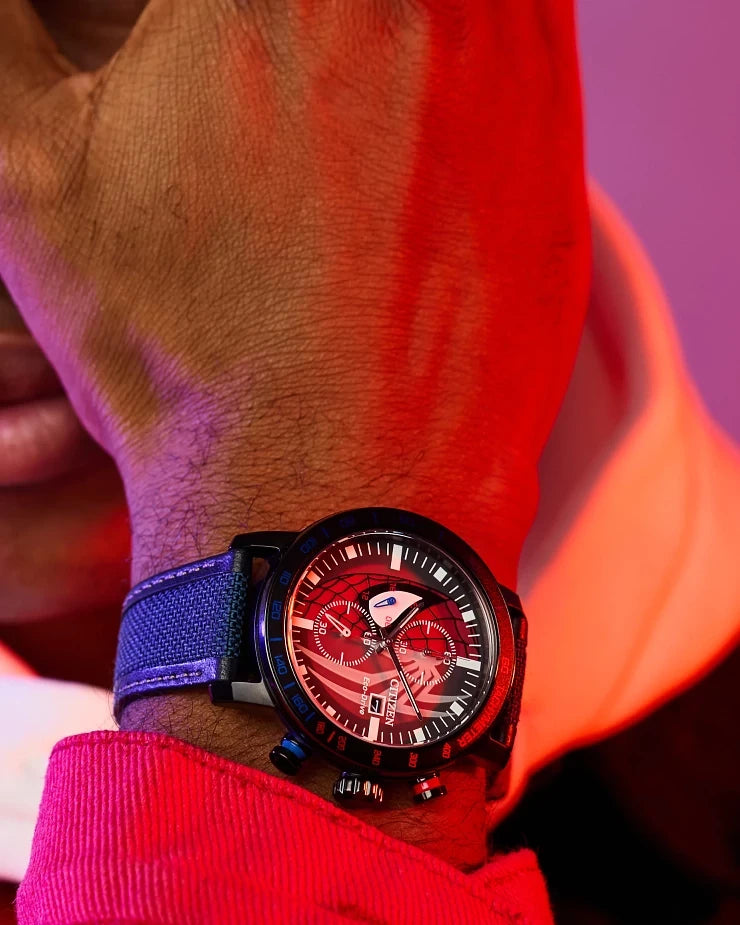 Close-up lifestyle image of the Citizen Spider-Man Double Vision CA0855-47W on wrist with dramatic red lighting, showing the divided Spider-Man dial, tachymeter bezel, and blue Cordura strap