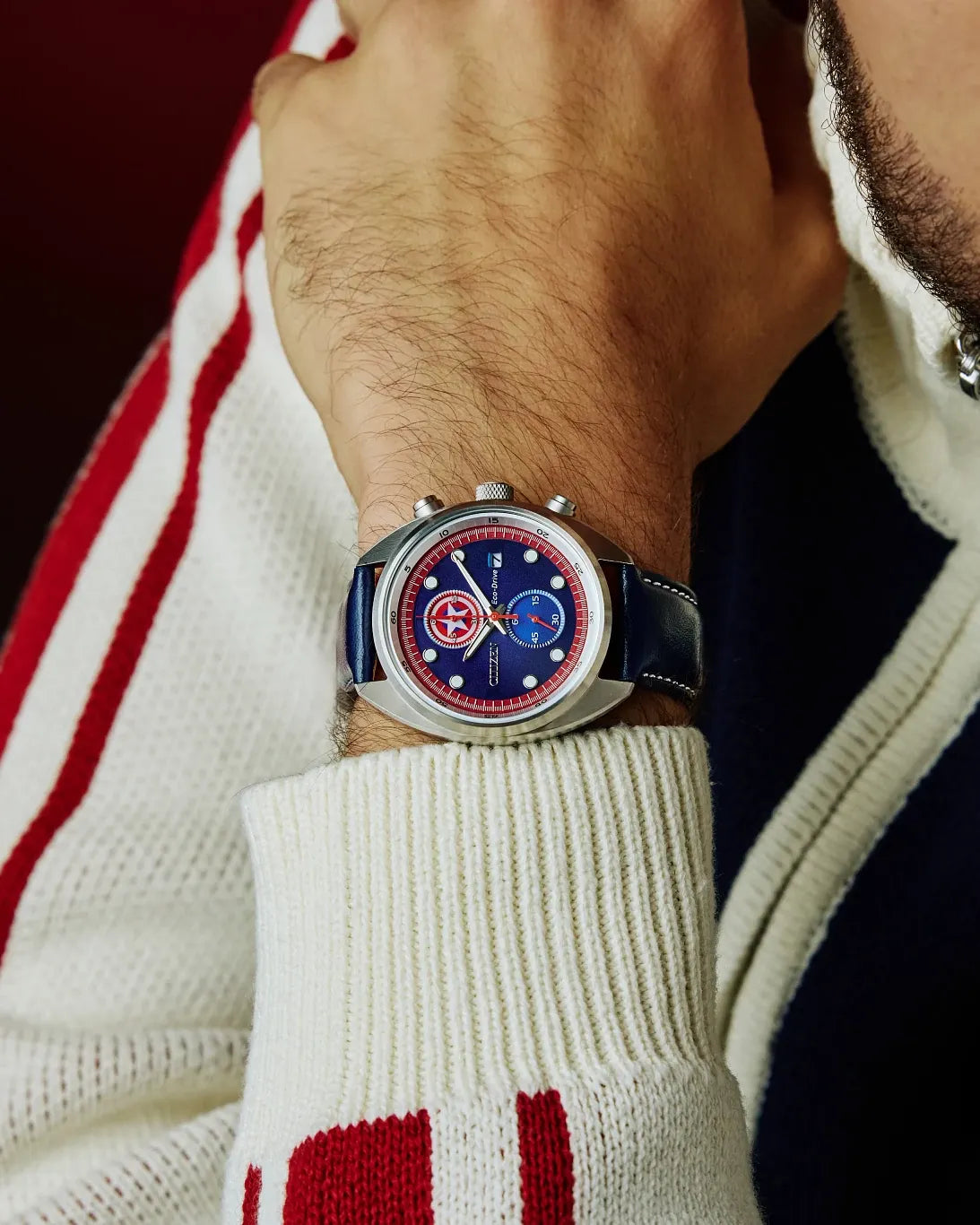 Close-up of a wrist wearing a watch with a red, white, and blue face, against a blurred background.
