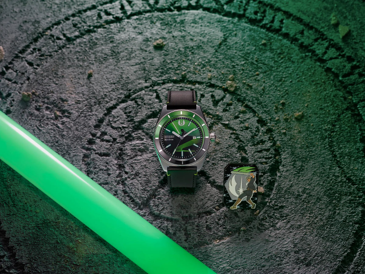Citizen Star Wars Luke Skywalker AW1910-48W displayed with collectible Jedi-inspired pin and green lightsaber background, featuring black and green dial, polished silver-tone case, and black leather strap.