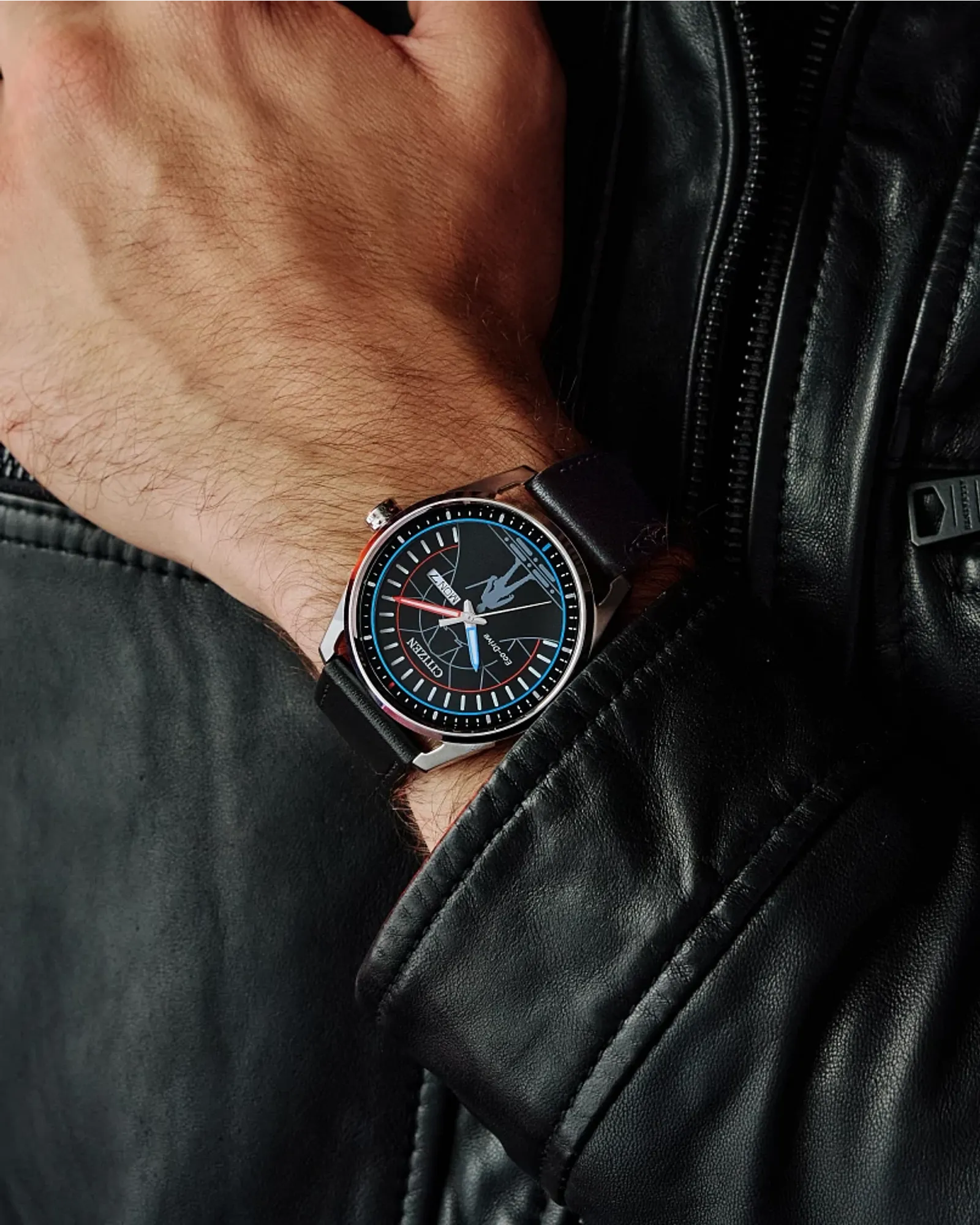 Close-up of a person wearing a black leather watch with a detailed face, against a black leather jacket background.