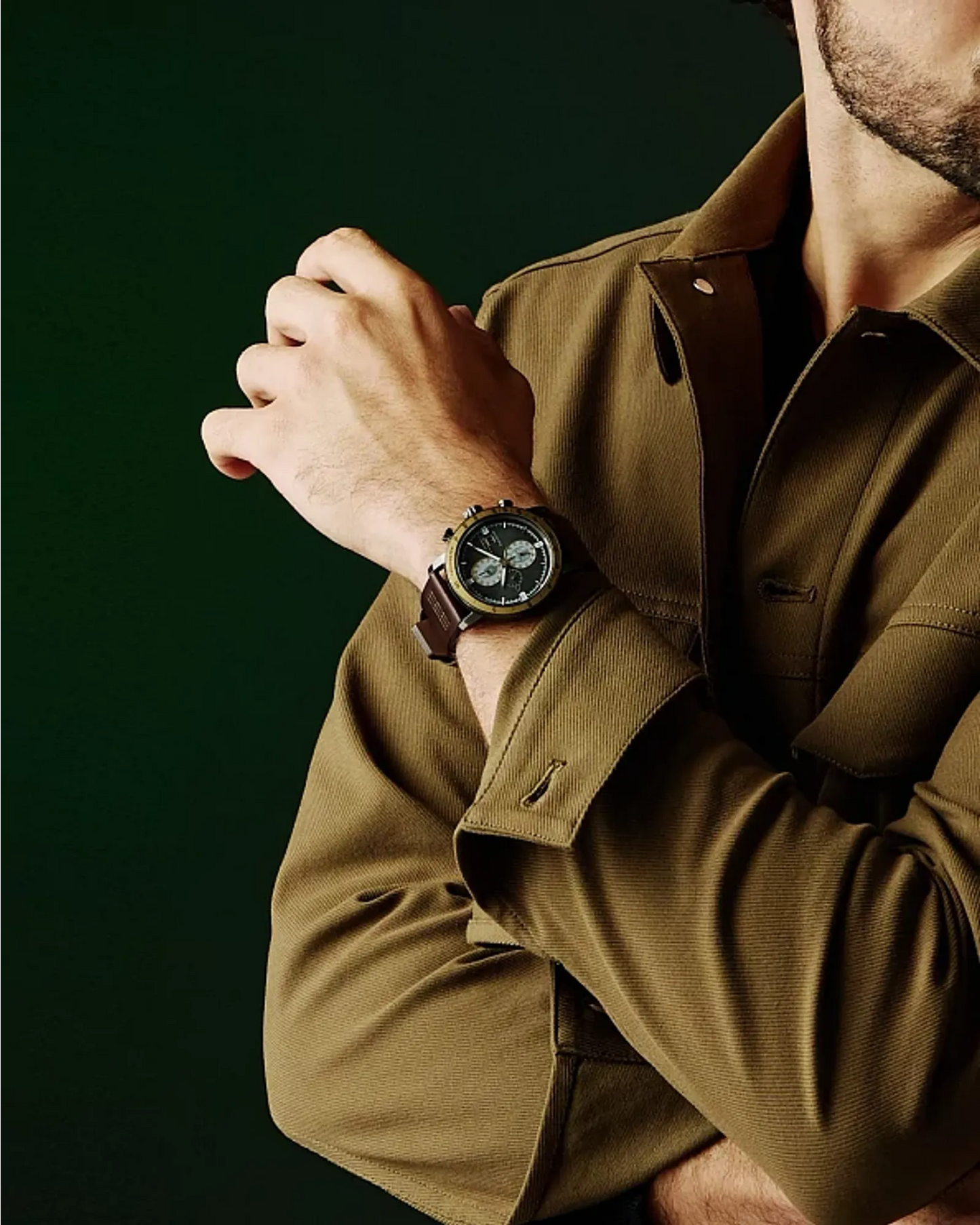 Man wearing a brown jacket and watch with a dark background