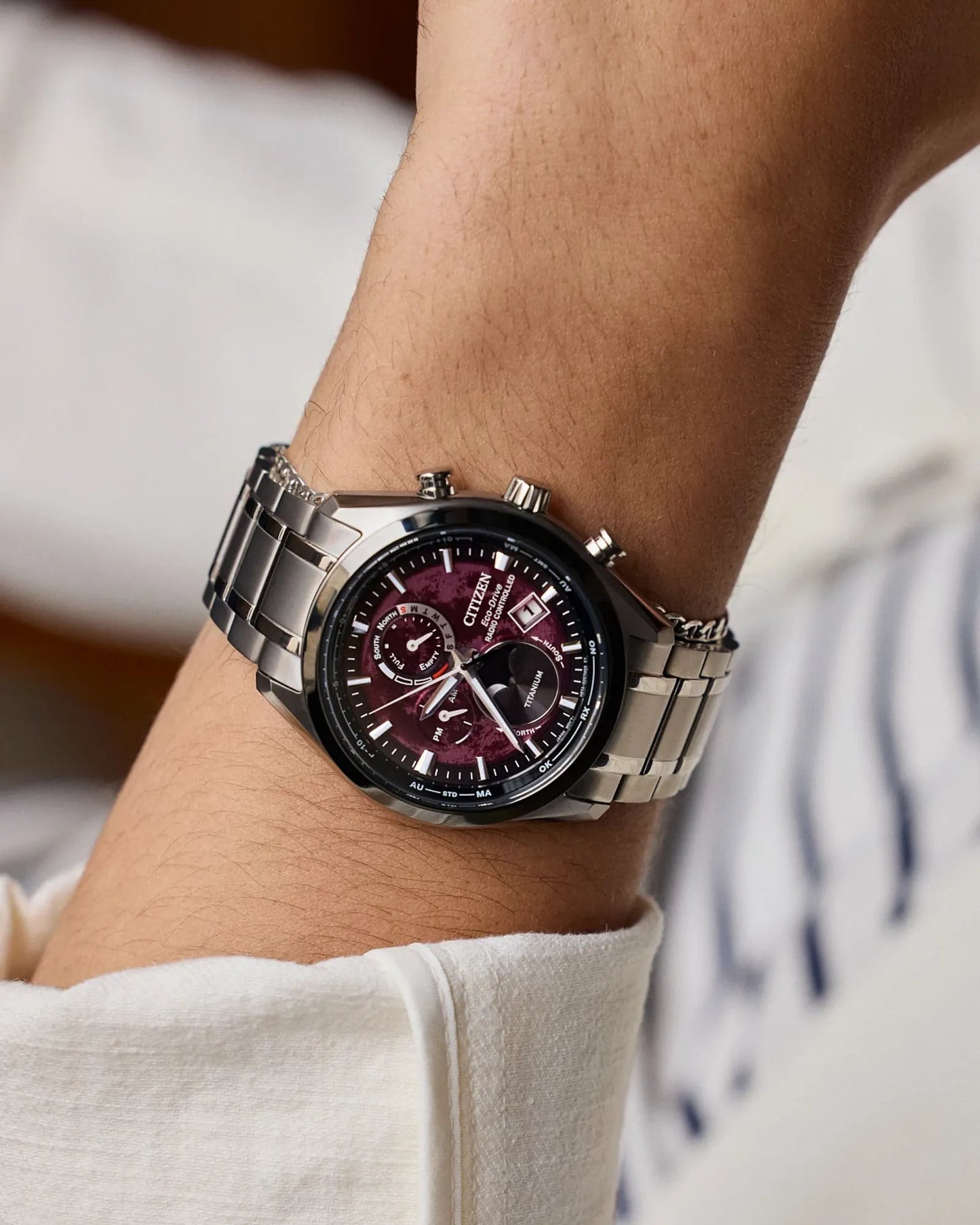 Close-up of a wrist wearing a silver watch with a maroon face.