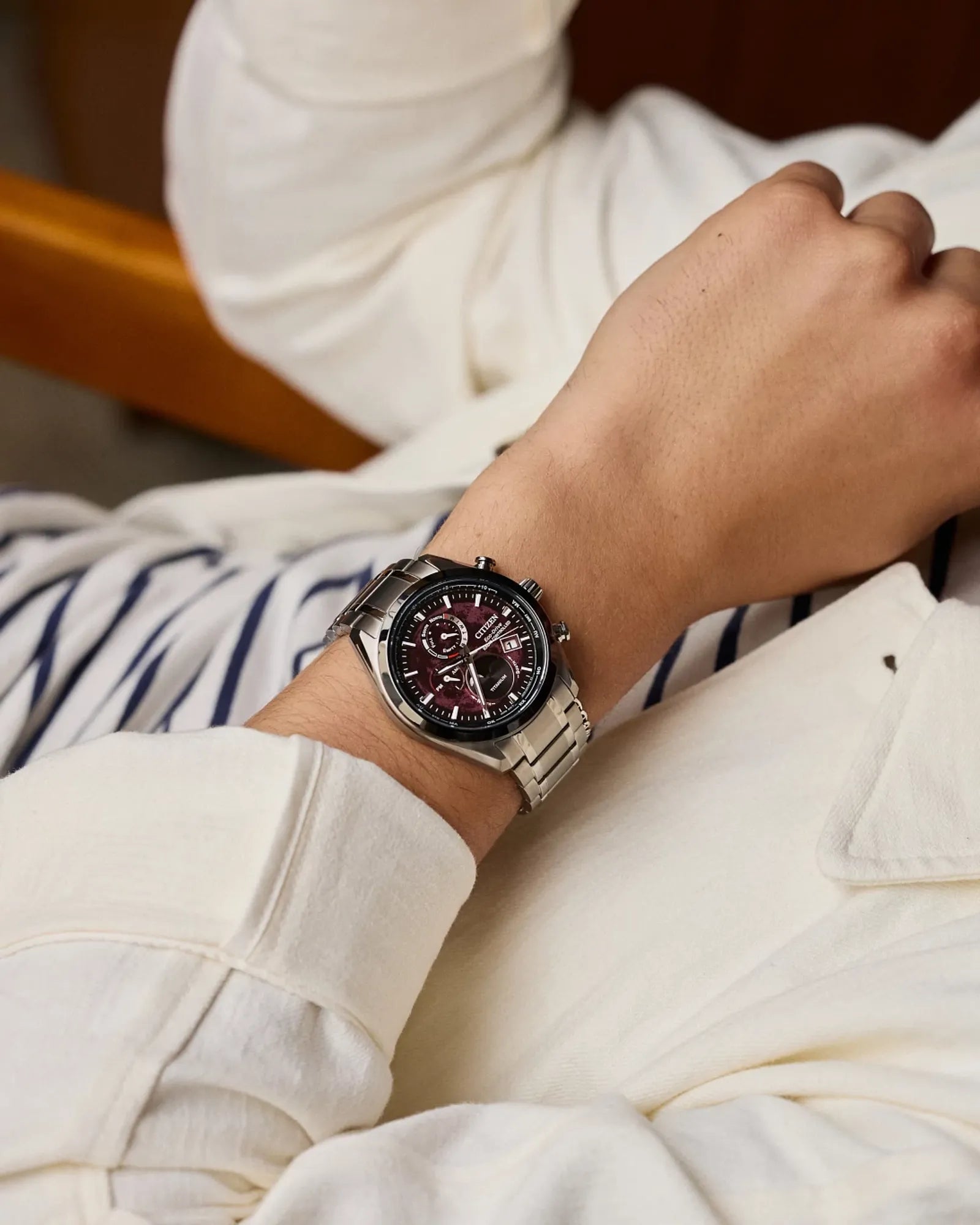 Person wearing a watch with a white jacket and striped shirt in the background