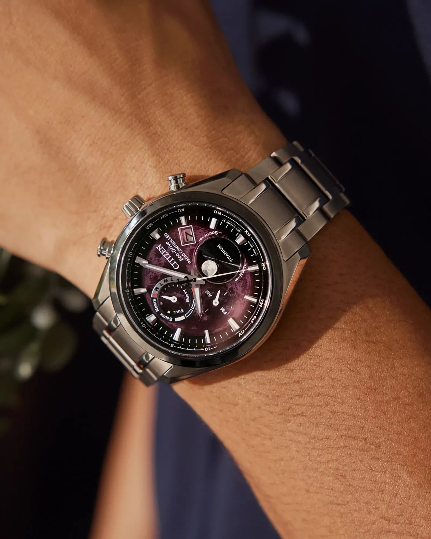 Silver watch with a dark face on a wrist against a blurred background