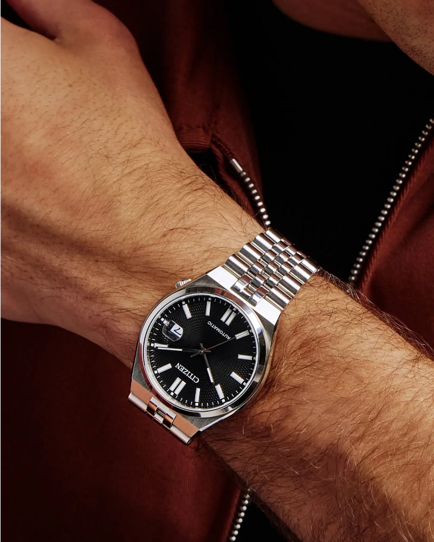 Silver watch with black dial on a wrist against a dark background
