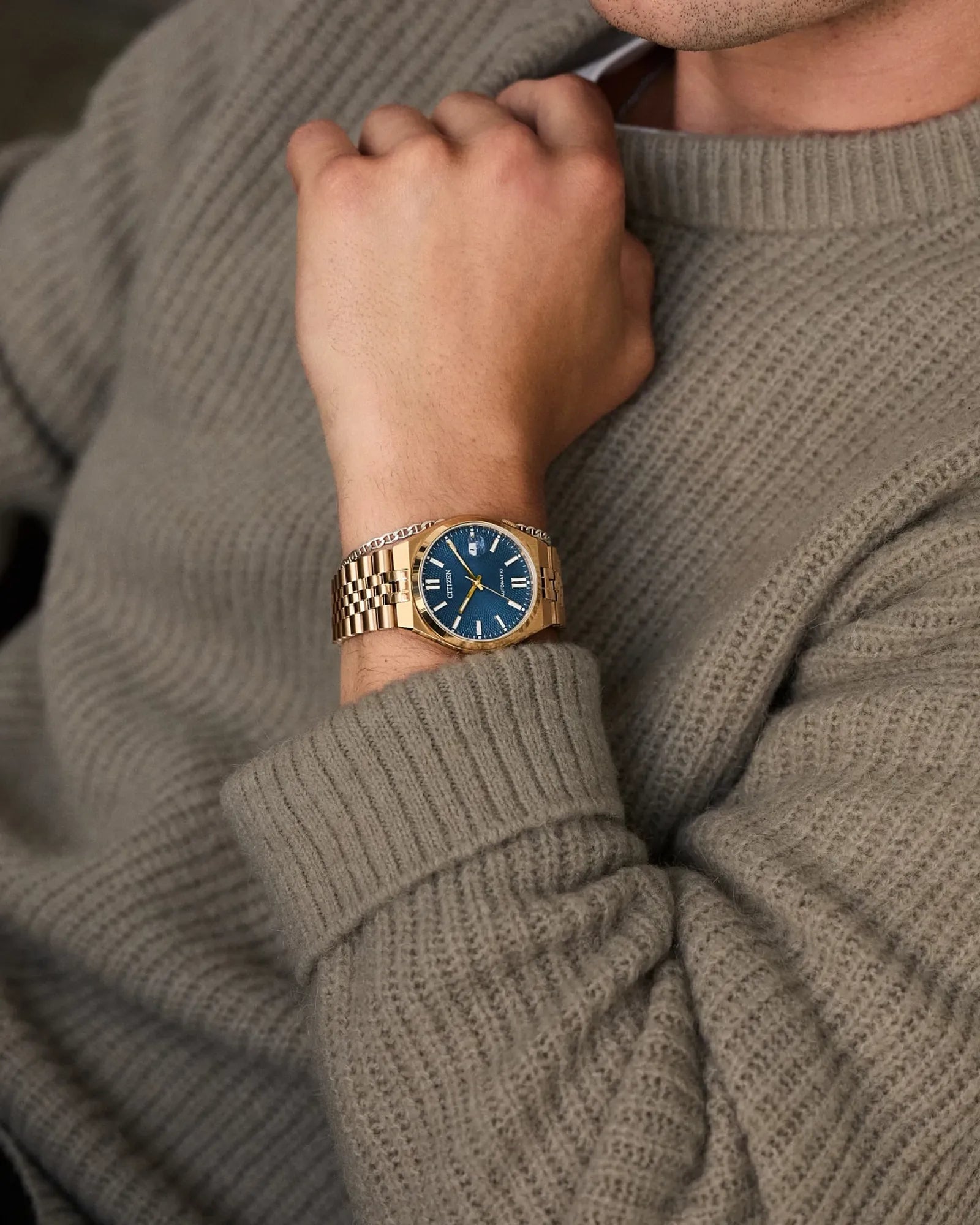 Person wearing a gold watch with a blue face on a gray sweater.