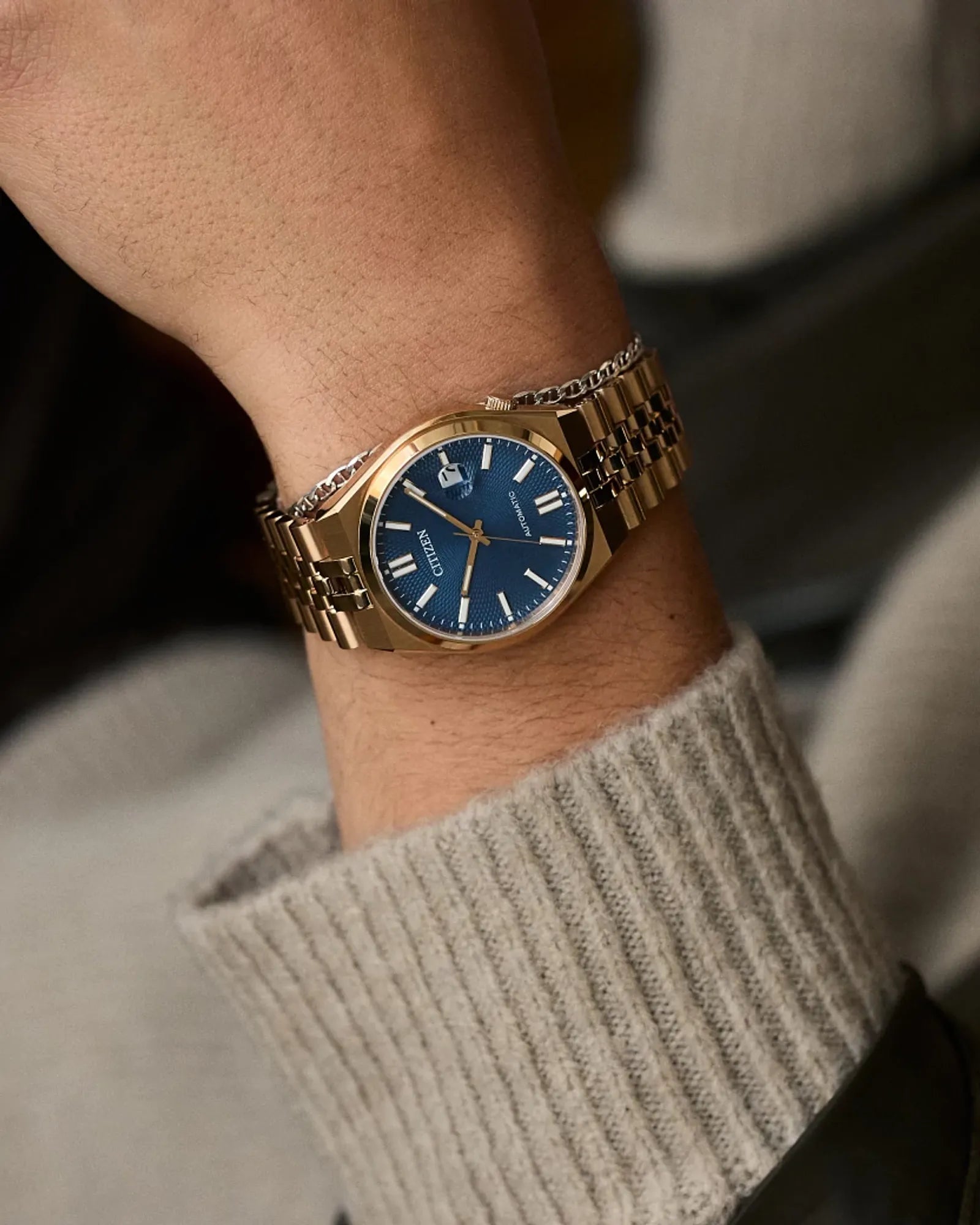 Gold watch with a blue face on a wrist, wearing a beige sweater.