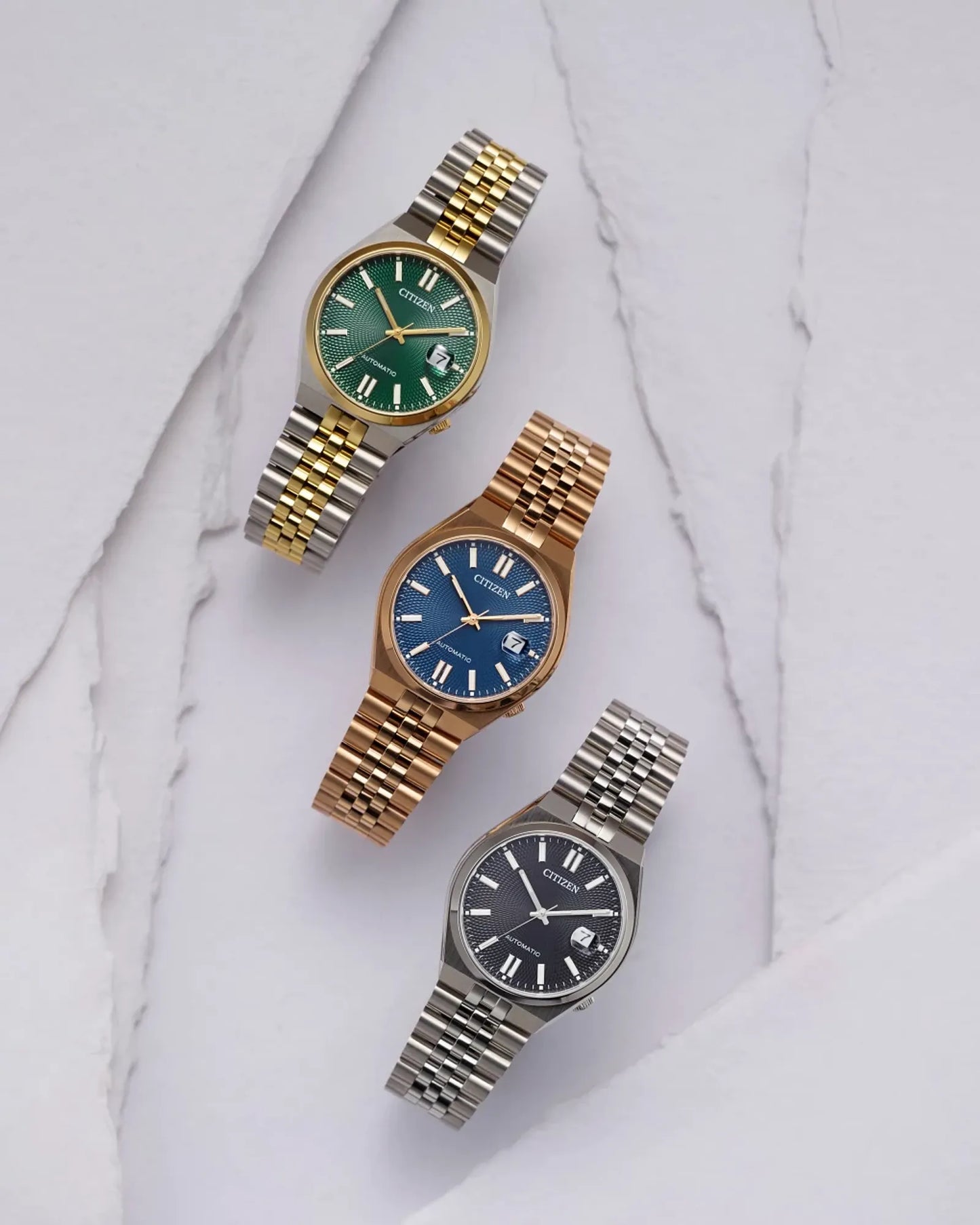 Three watches with different colored faces and metal bands on a marble surface