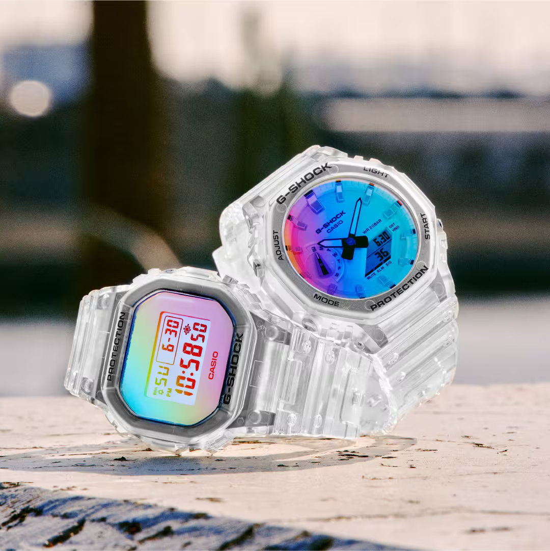 Two clear G-Shock watches with colorful displays on a wooden surface.