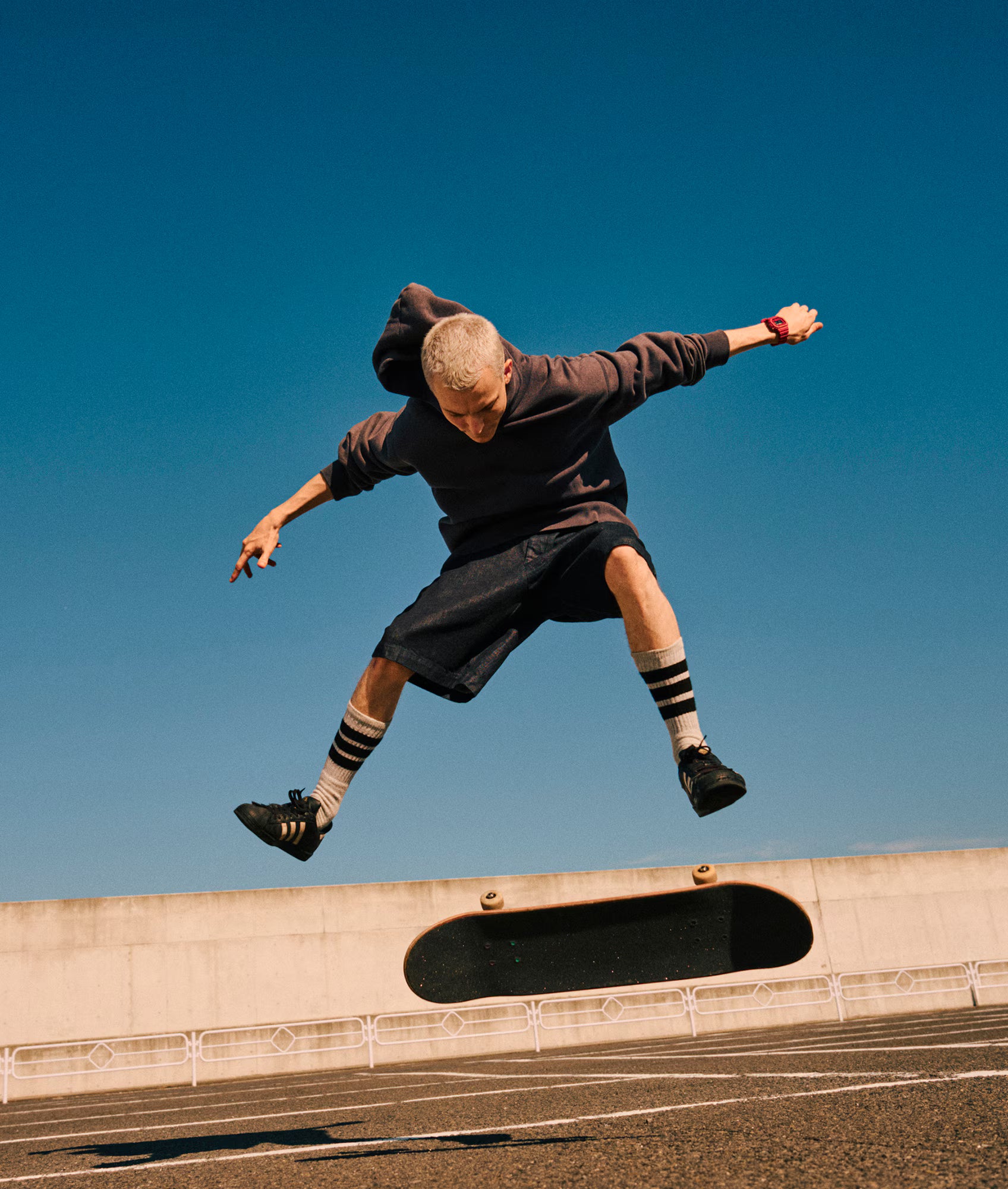 Person in a hoodie and shorts jumping in the air with a clear blue sky background