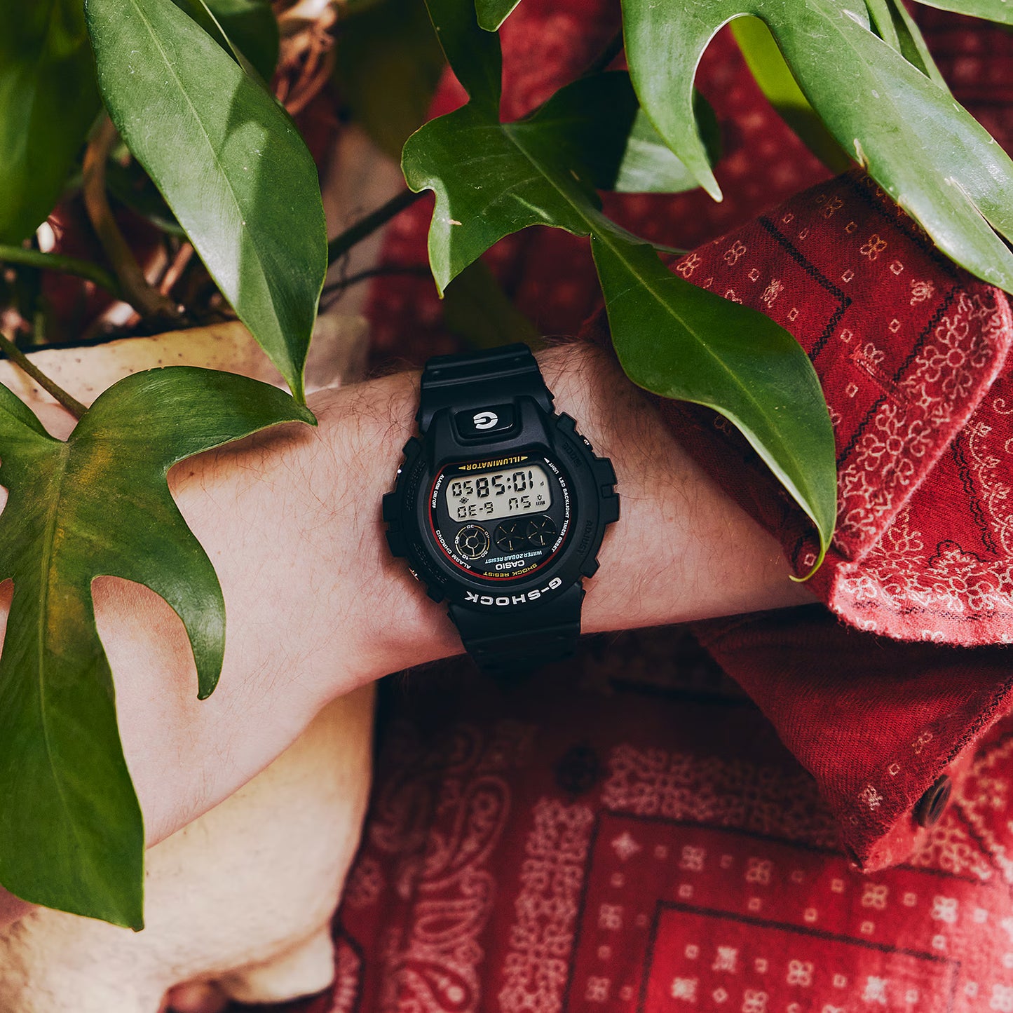 Person wearing a Casio G-Shock digital watch with green leaves in the foreground