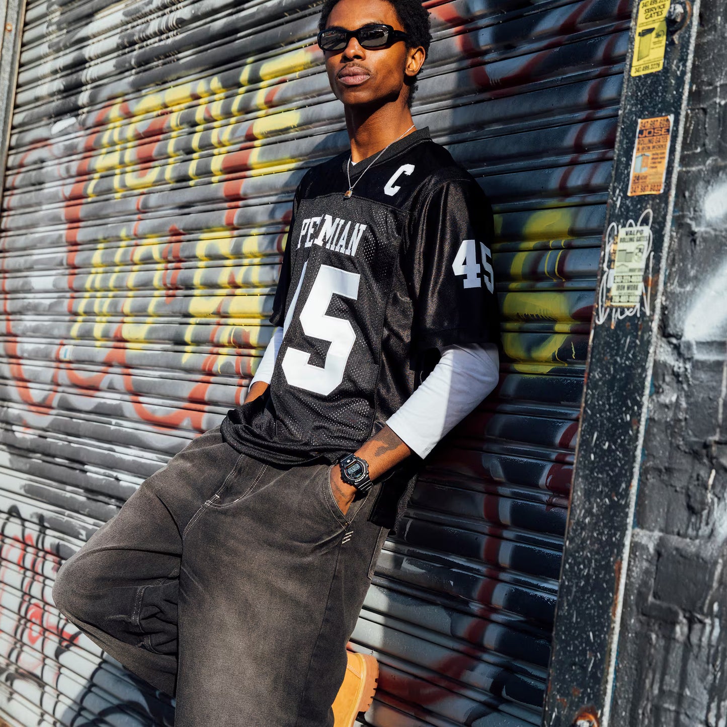 Person wearing a sports jersey leaning against a graffiti-covered wall