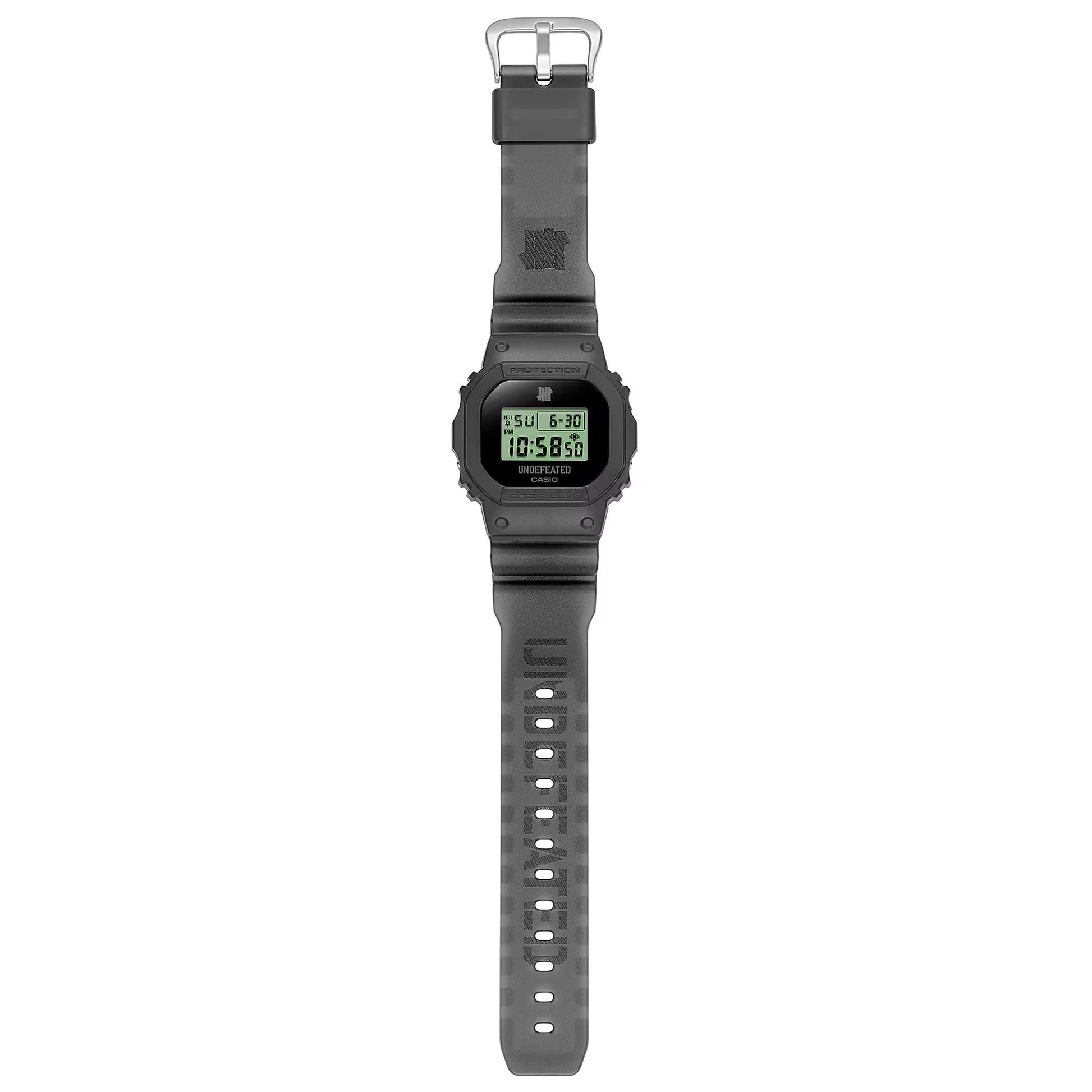 Casio G-SHOCK DWE5600UD-1 UNDEFEATED collaboration model with matte black Carbon Core Guard case, semi-translucent resin band featuring UNDEFEATED logo, green LCD display, engraved caseback, and special packaging. Includes two interchangeable camouflage straps (tiger camo, storm camo). Features shock resistance, mineral glass, 200m water resistance, LED Super Illuminator backlight, stopwatch, countdown timer, alarms, flash alert, auto-calendar, and ±15 sec/month accuracy. Case size 48.9 × 43.8 × 13.7 mm, we