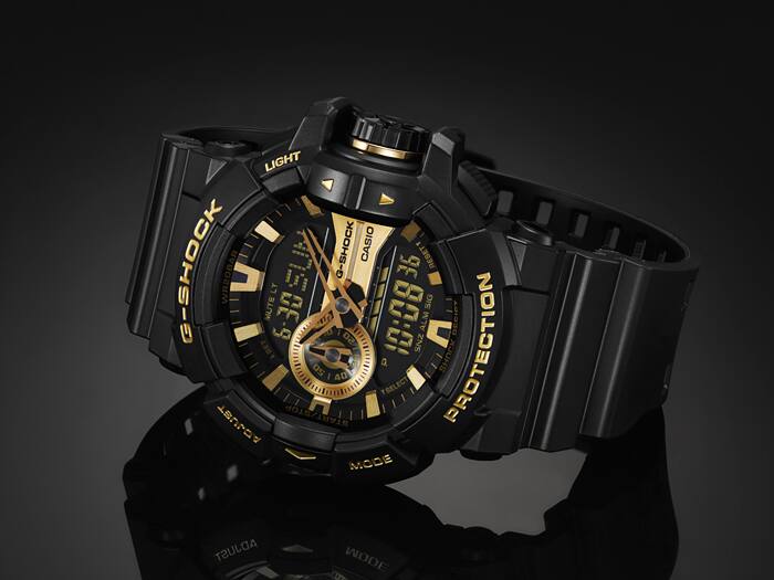 Black and gold G-Shock watch on a reflective surface with a dark background