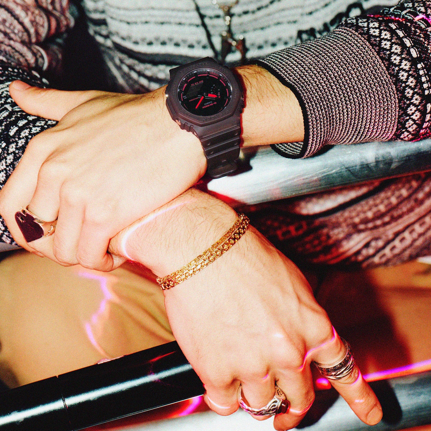 Close-up of hands with a black watch and gold bracelet, wearing rings, on a blurred background.