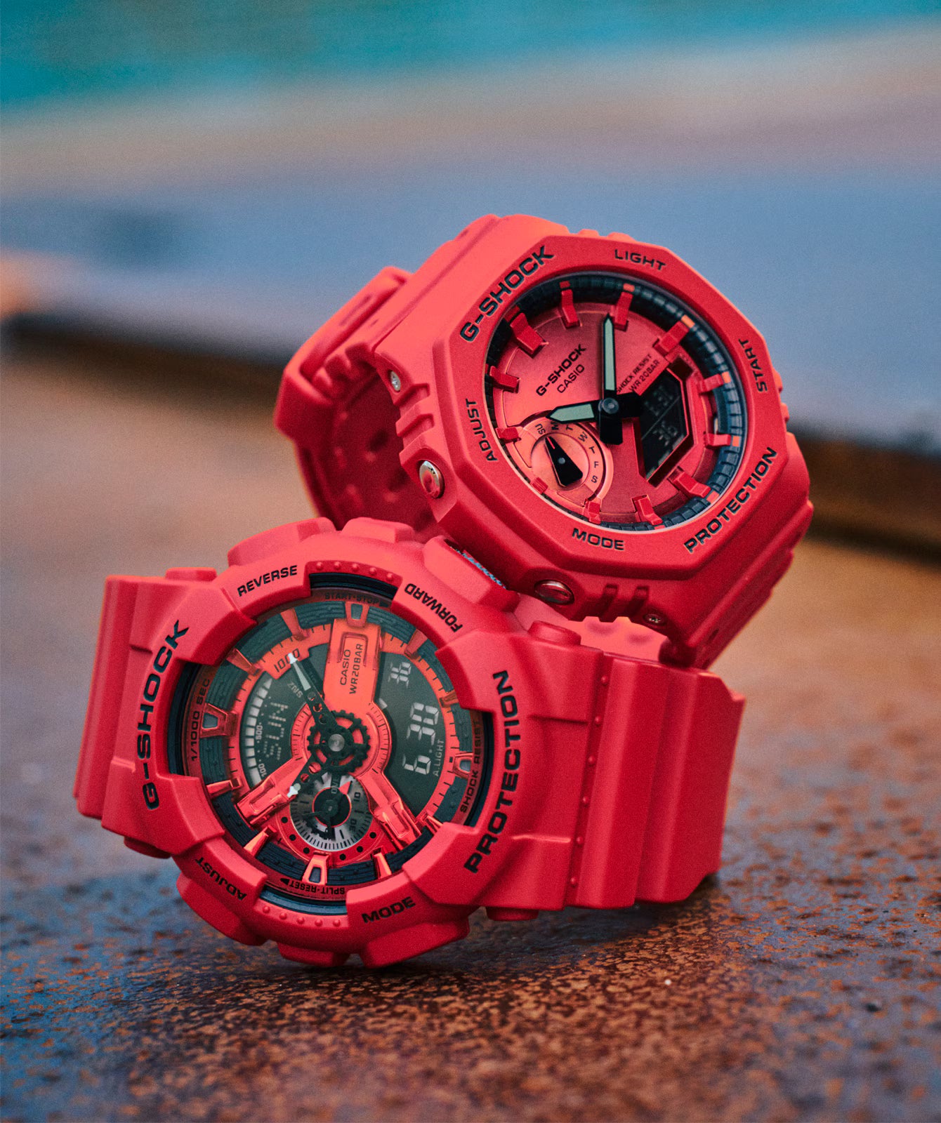 Two red Casio G-Shock watches on a textured surface with a blurred background