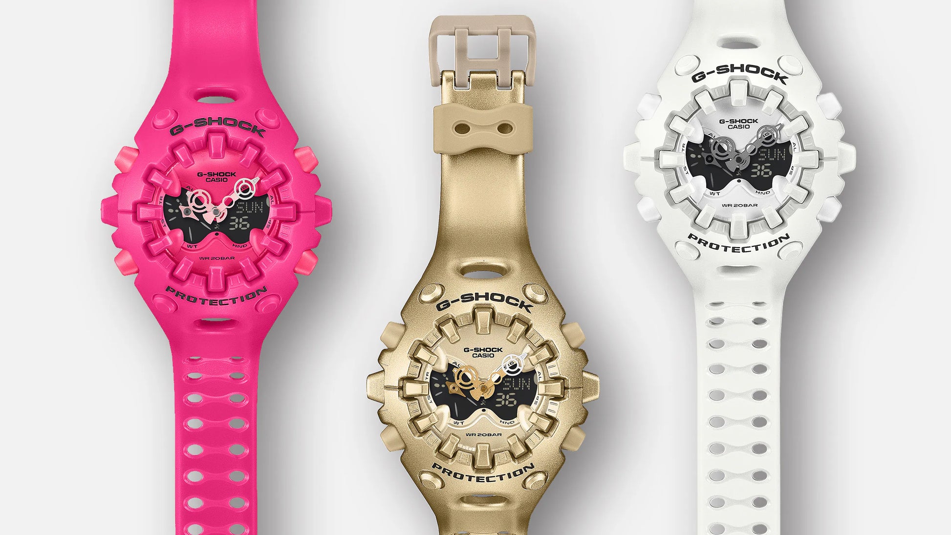 Three G-Shock watches in pink, gold, and white on a light gray background