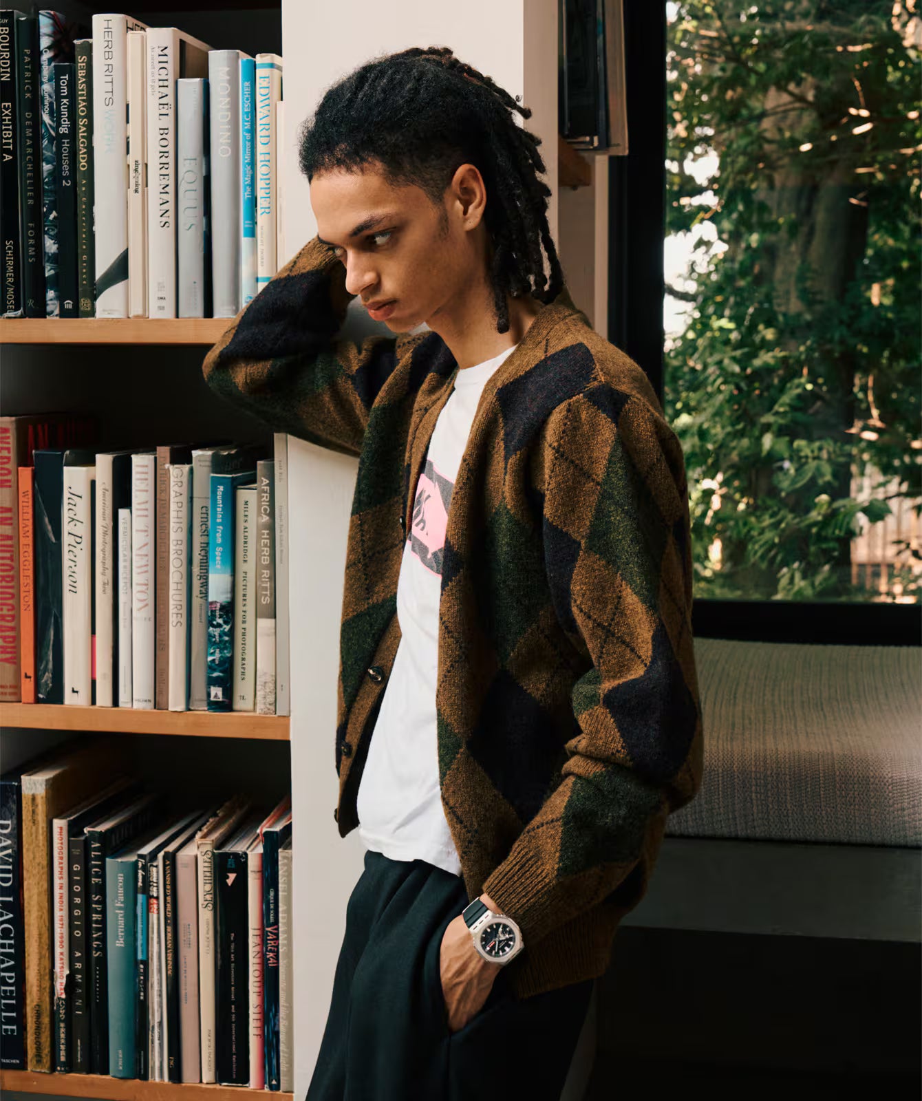 Person wearing a patterned cardigan in a room with bookshelves and a window.