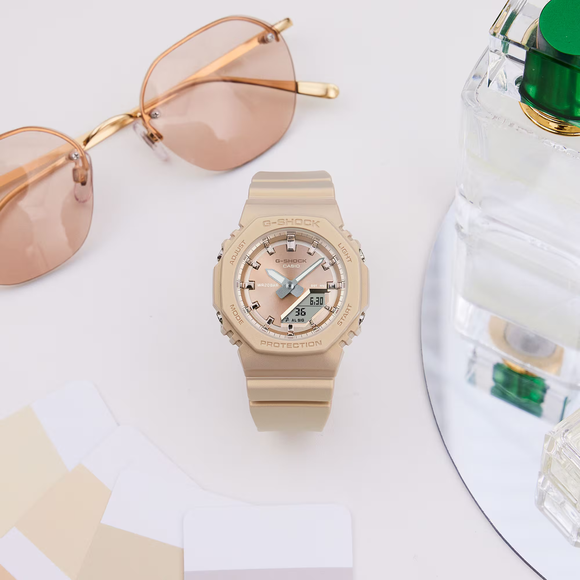 Beige Casio watch with sunglasses and perfume bottle on a white surface