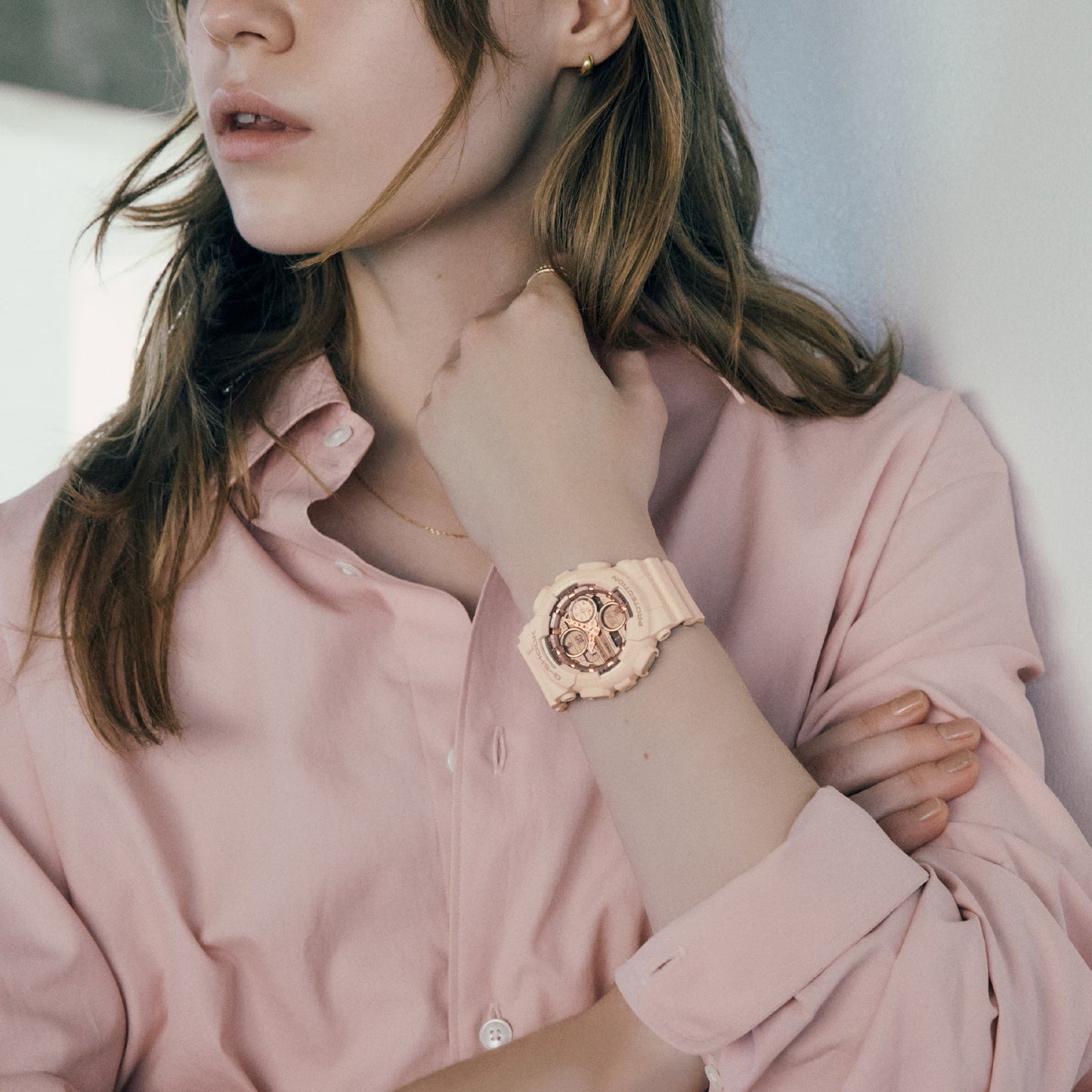 Woman wearing a pink watch and shirt, adjusting her necklace.