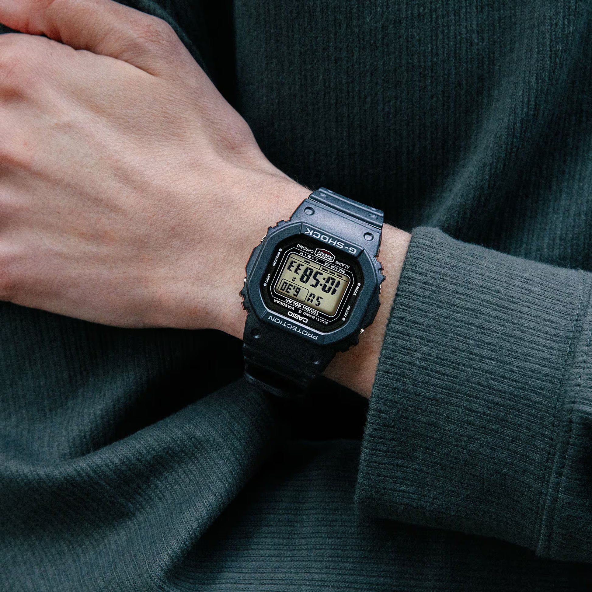 Person wearing a black digital watch on a dark background