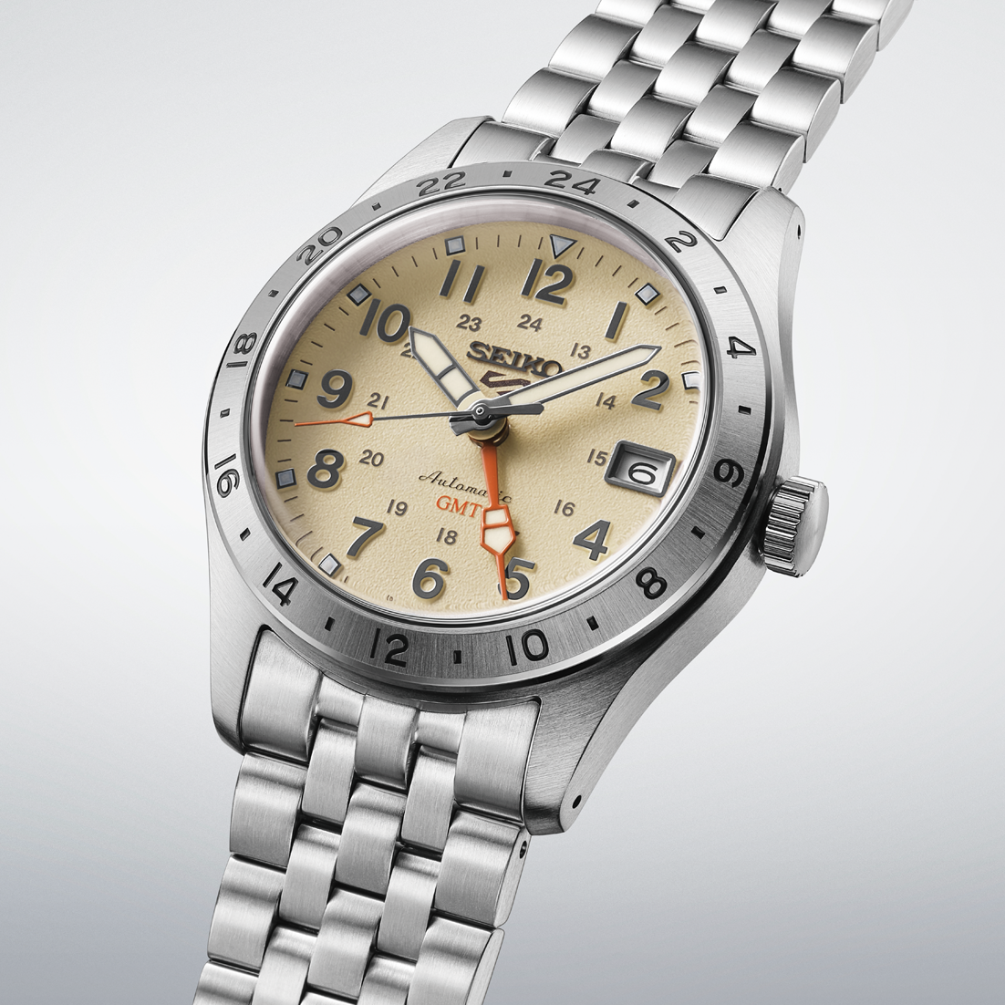 A Seiko wristwatch with a stainless steel link bracelet, featuring a beige dial with black Arabic numerals, a silver bezel, and a date window.