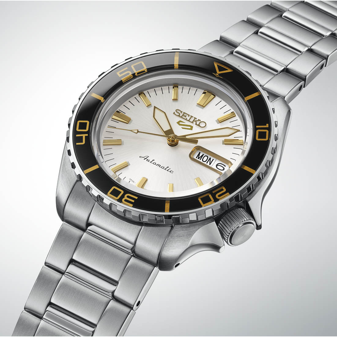 Close-up of SEIKO 5 Sports HDB004 showing white sunray dial, gold-tone hands and indexes, black rotating bezel, crown, and stainless steel bracelet.