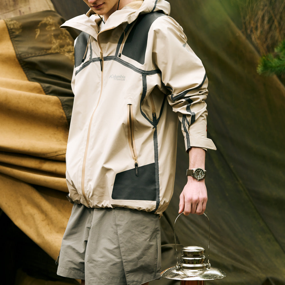 Person wearing a beige and black jacket holding a lantern with a tent in the background