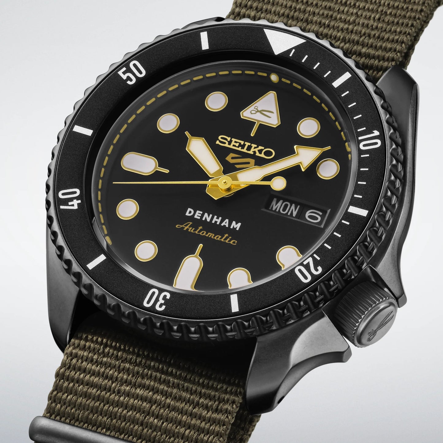 SEIKO 5 Sports SBSA283 DENHAM Limited Edition – black sunray dial with gold accents, stitching-inspired motif, black/gray rotating bezel, green nylon strap, automatic movement, and 100m water resistance.