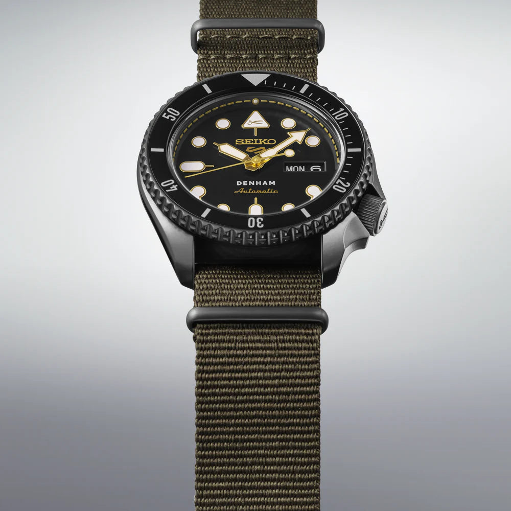 SEIKO 5 Sports SBSA283 DENHAM Limited Edition – black sunray dial with gold accents, stitching-inspired motif, black/gray rotating bezel, green nylon strap, automatic movement, and 100m water resistance.