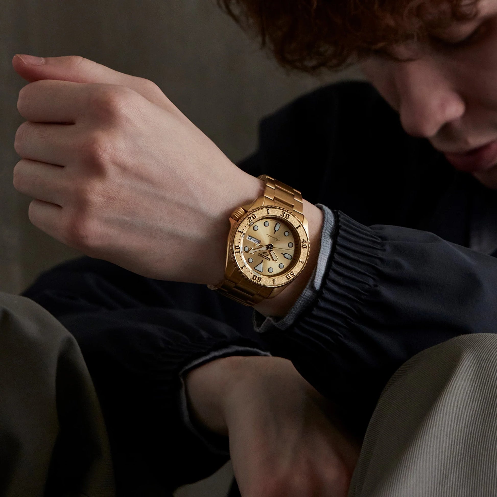 Person wearing a gold wristwatch with a detailed face.