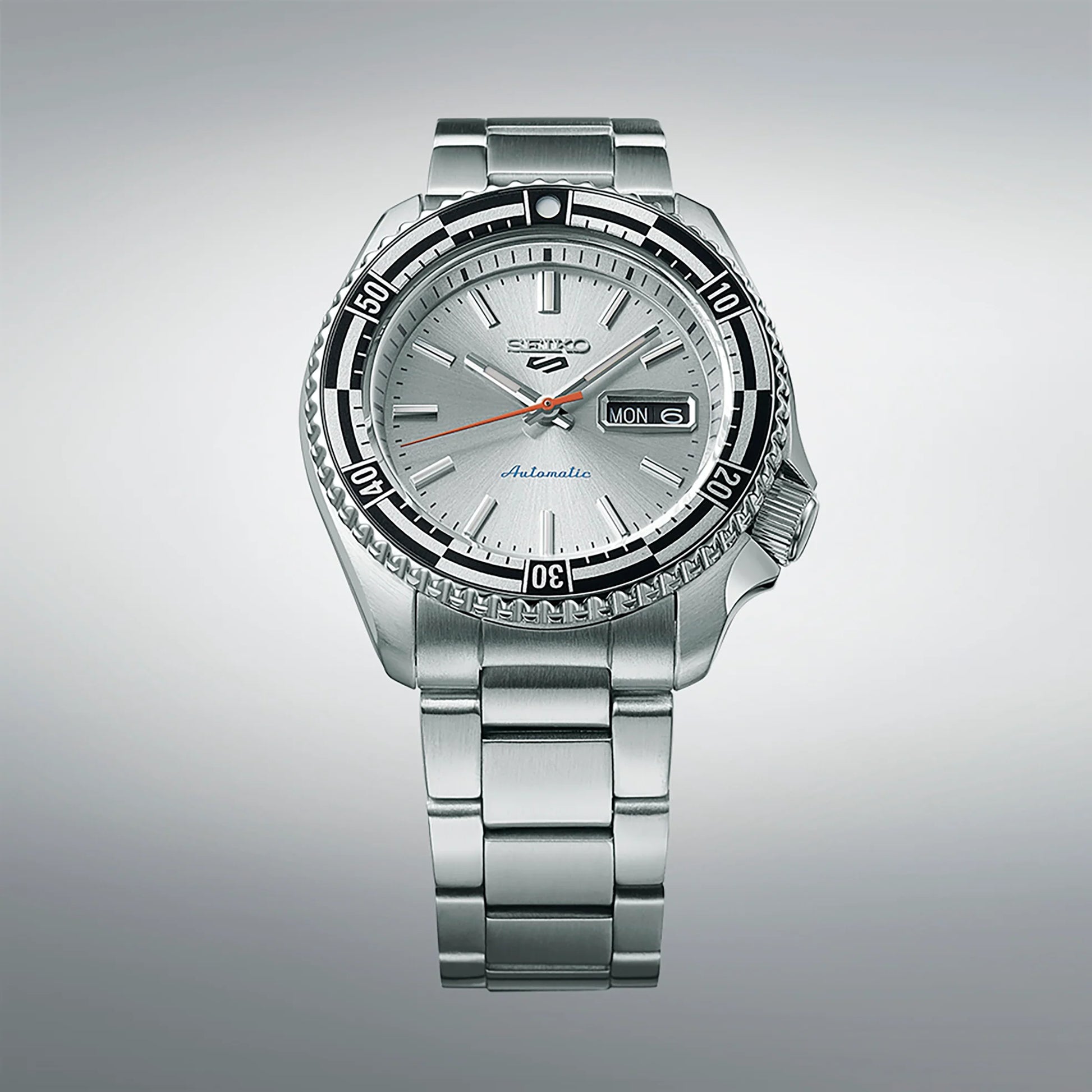 Seiko 5 Sports 55th Anniversary Special Edition automatic men's watch with silver dial, black and silver checkered rotating bezel, red-orange second hand, and stainless steel bracelet, inspired by the 1960s Seiko 5126-8130 model, available at Miseki Jewelry