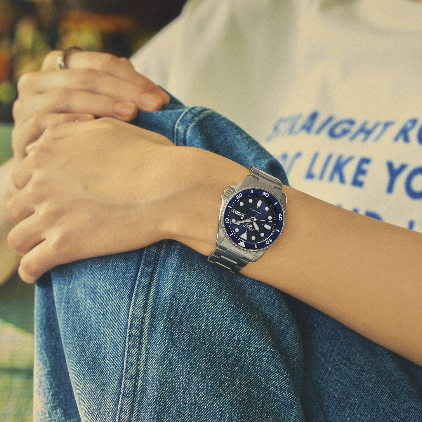 Person wearing a silver watch with a blue face on a blurred background