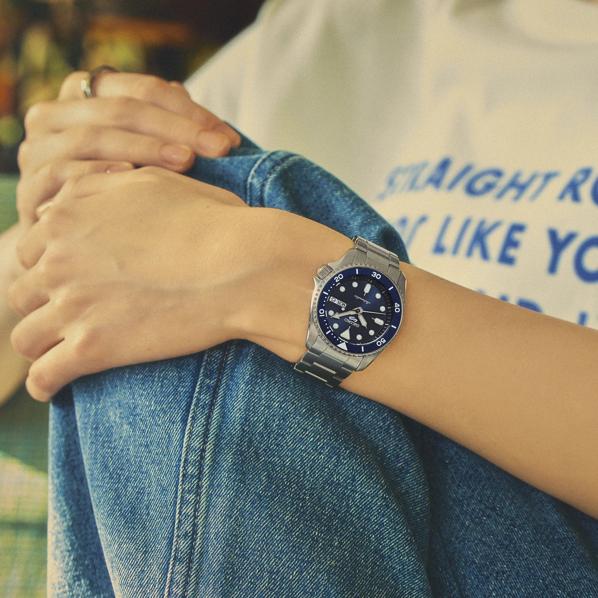 Person wearing a silver watch with a blue face on a blurred background