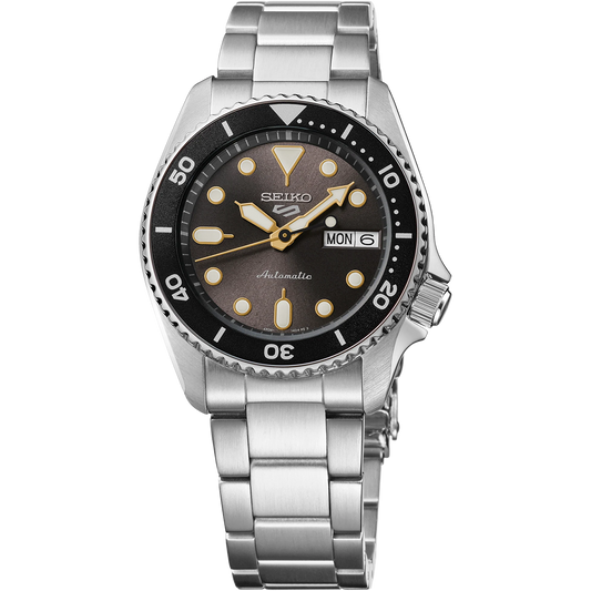 Seiko 5 Sports SRPL79 SKX Mid-Size automatic watch with 38 mm stainless steel case, charcoal gray dial with gold-tone accents, black unidirectional rotating bezel, Hardlex crystal, luminous hands and markers, stainless steel three-row bracelet with tri-fold clasp, and screwdown see-through caseback. Powered by Caliber 4R36 automatic movement with 24 jewels, 41-hour power reserve, and day/date display. Water resistant to 100 meters.