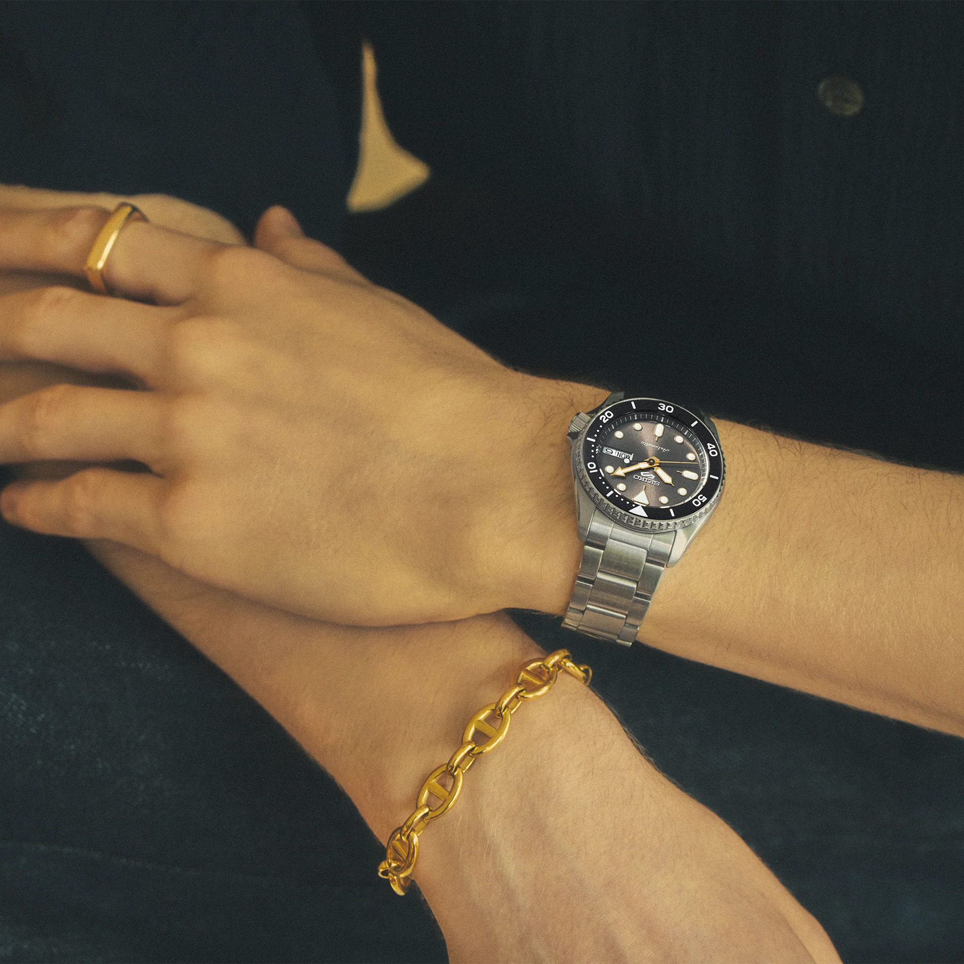 Close-up of a wrist wearing a silver watch with a gold bracelet and ring.