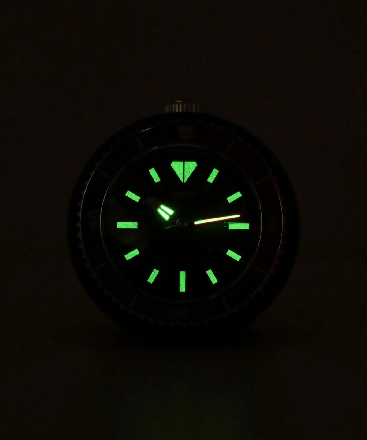 SEIKO QHE207LLH rotating bezel alarm clock illuminated in the dark with green built-in dial light and luminous watch-style markers.