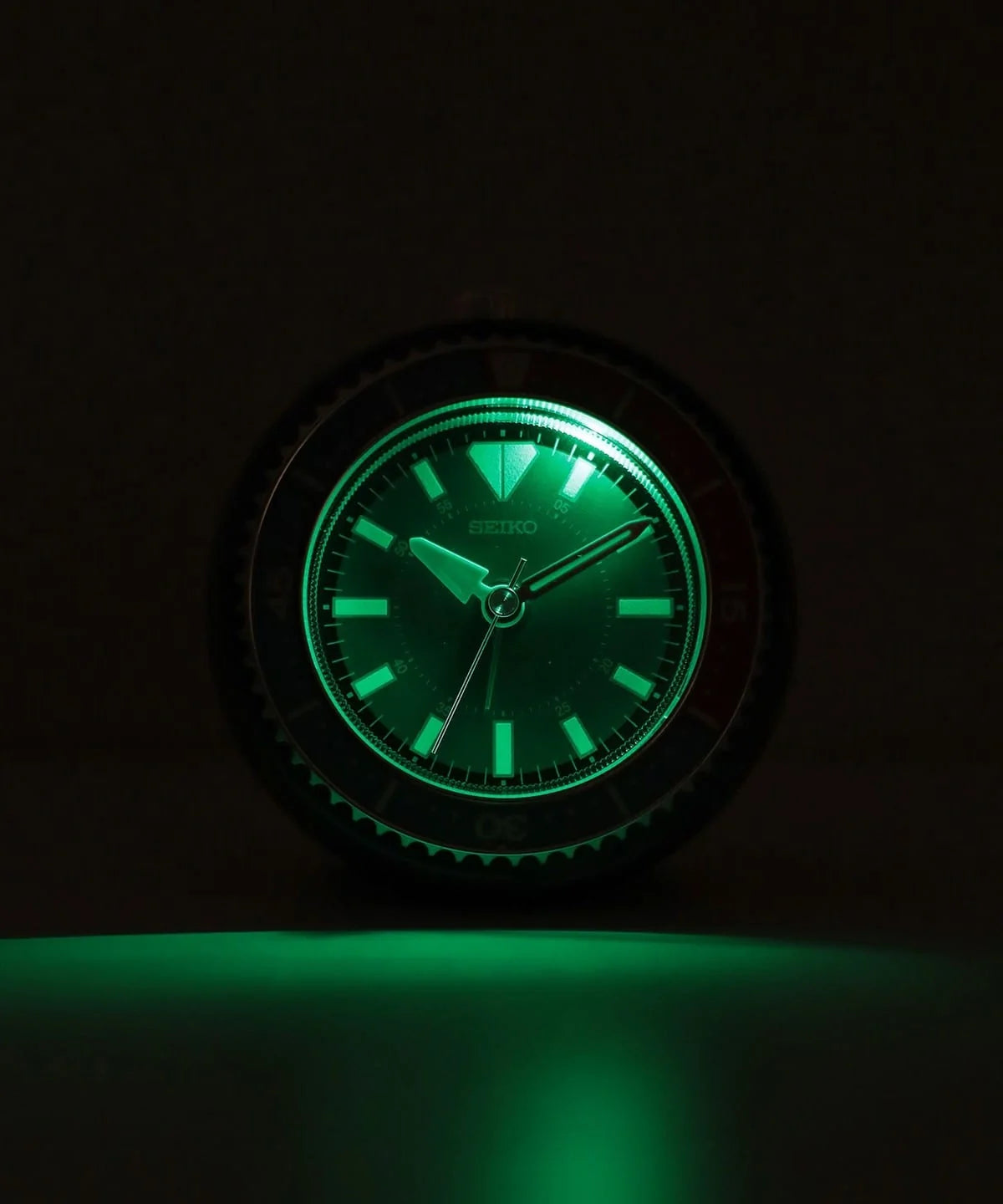SEIKO QHE207LLH blue rotating bezel alarm clock displayed on magazines with earbuds, a desk lamp, and retro lifestyle accessories.