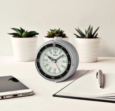 SEIKO QHE207SLH rotating bezel desk alarm clock displayed on a modern workspace with plants, notebook, pen, and smartphone.